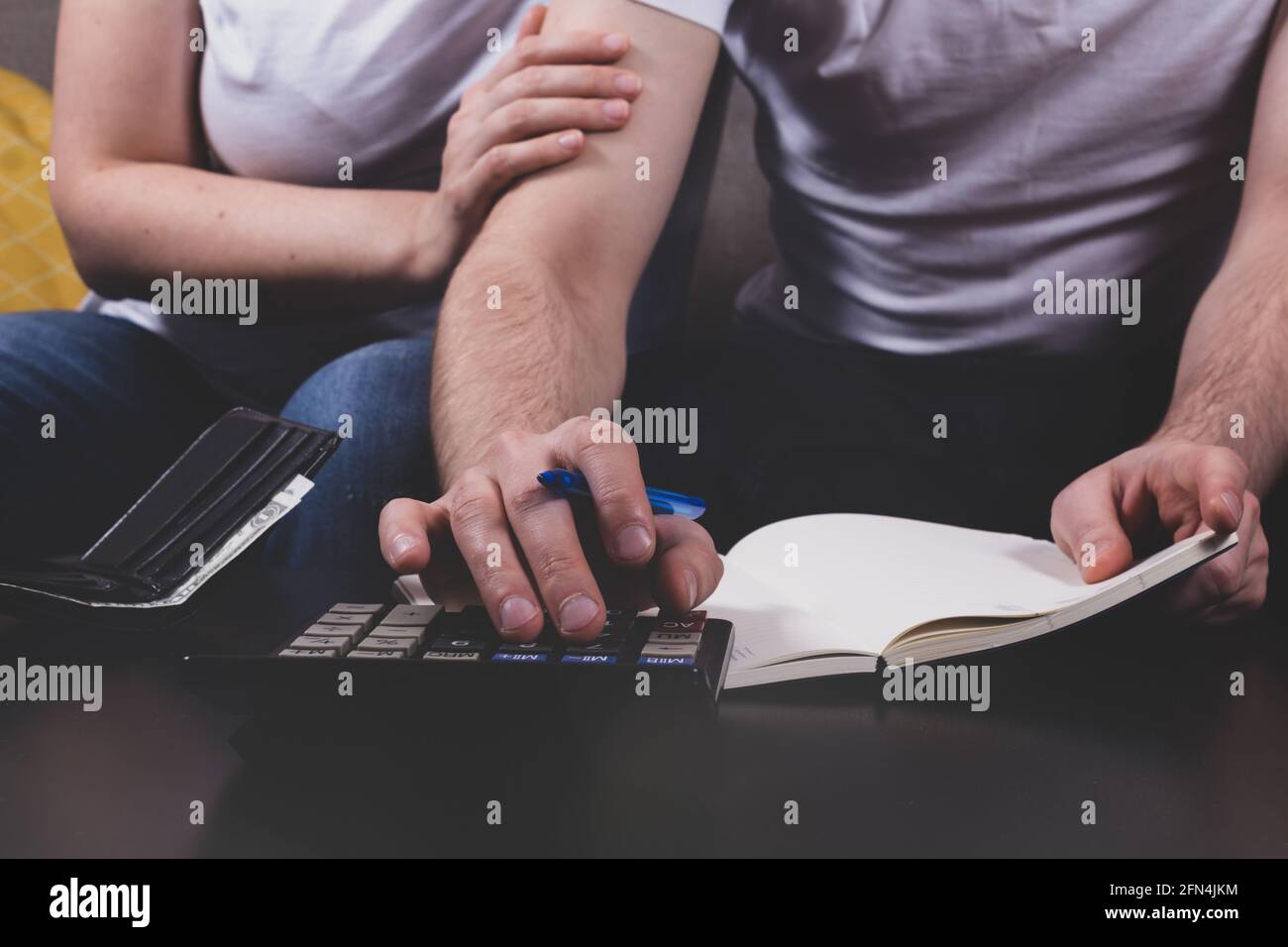 Giovane coppia che calcola il budget di famiglia seduto insieme sul divano. La moglie sostiene il marito in tempi difficili. Concetto di crisi finanziaria familiare. Foto Stock