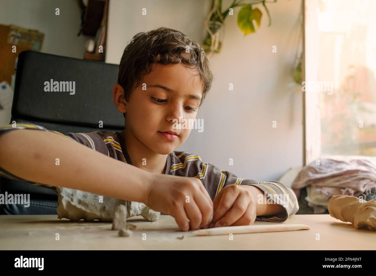 bambino che gioca con l'argilla a casa durante la quarantena. ragazzo focalizzato che crea forme con le mani e utilizza creatività e abilità manuali per modellare forme di giocattoli Foto Stock