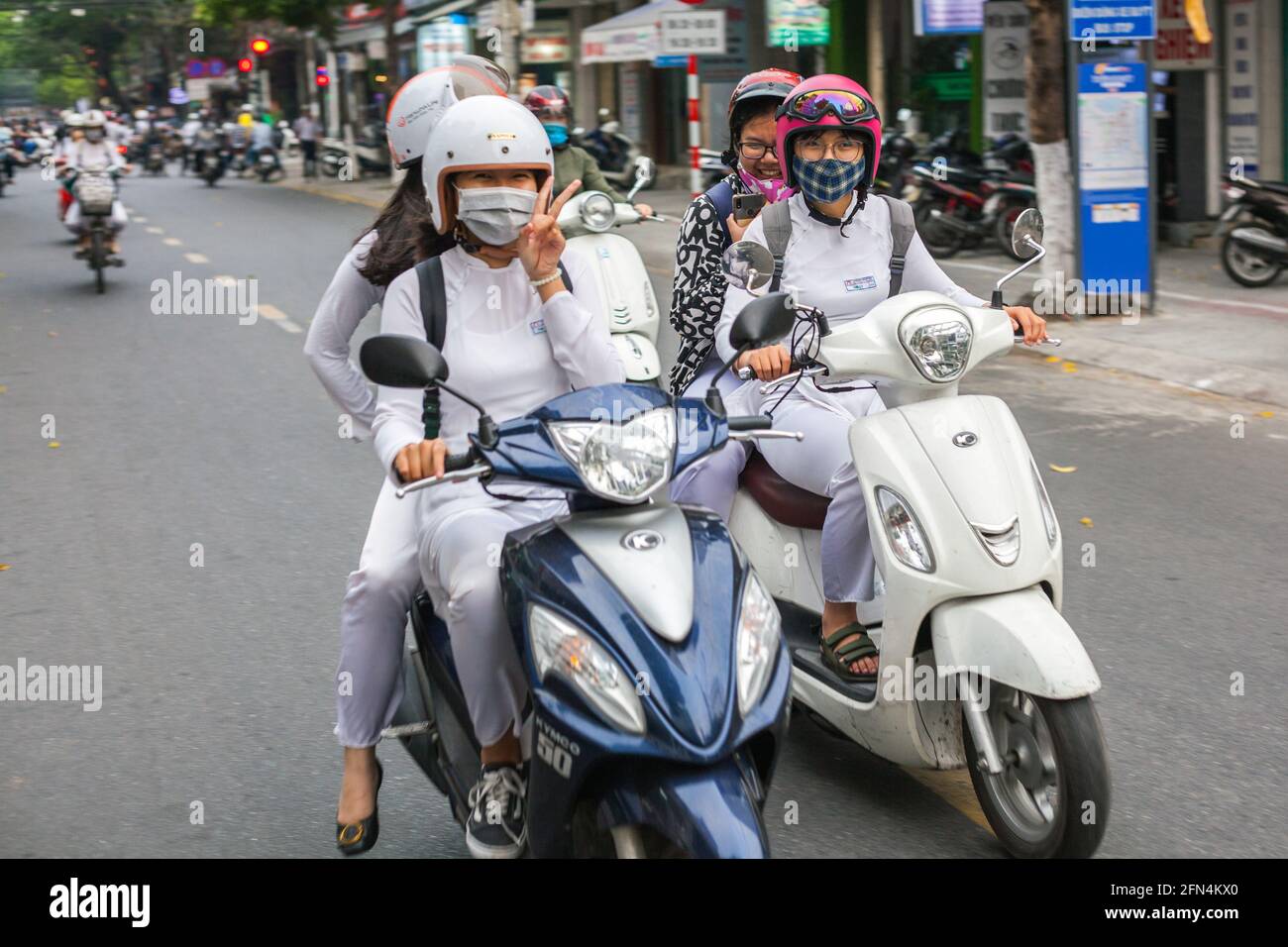 Graziose studentesse vietnamite che indossano abiti tradizionali bianchi ao dai siedono su scooter dando segno di pace, da Nang, Vietnam Foto Stock