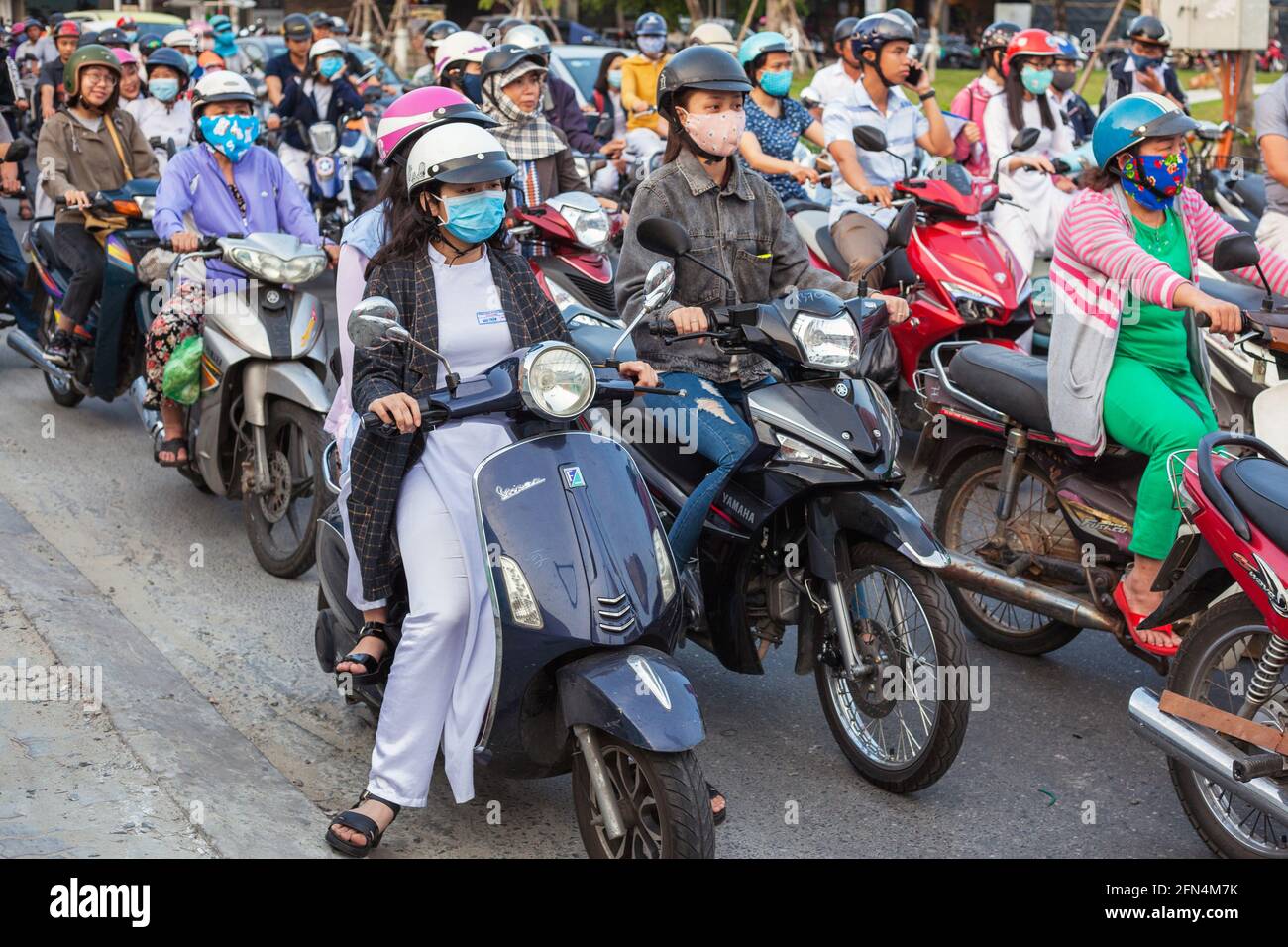 Graziose studentesse vietnamite che indossano abiti tradizionali bianchi ao dai siedono sugli scooter alla giunzione in attesa di luci da cambiare, da Nang, Vietnam Foto Stock