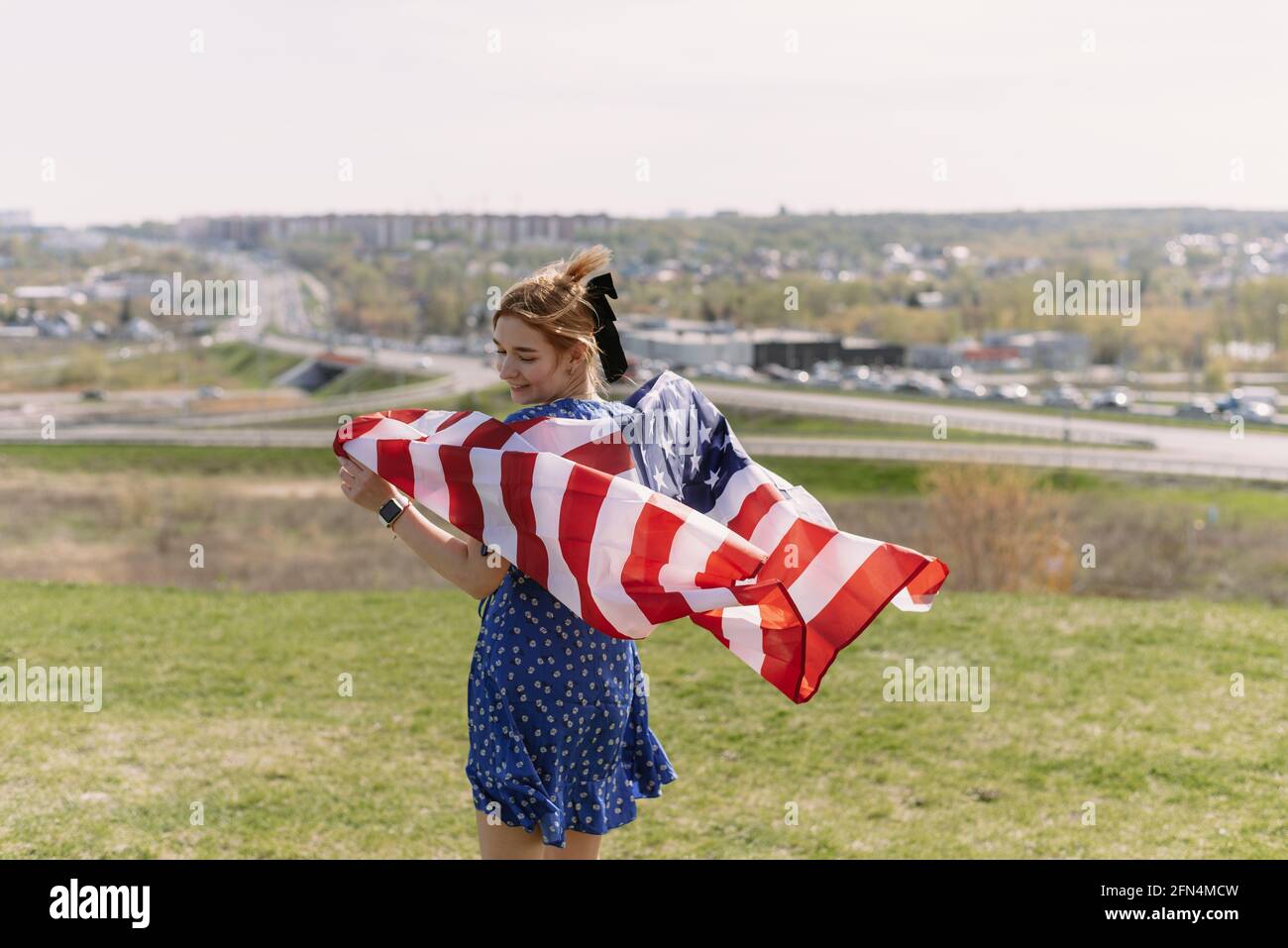 Una giovane donna con la bandiera nazionale degli Stati Uniti sulle sue spalle sullo sfondo della città celebra Il giorno dell'Indipendenza degli Stati Uniti Foto Stock