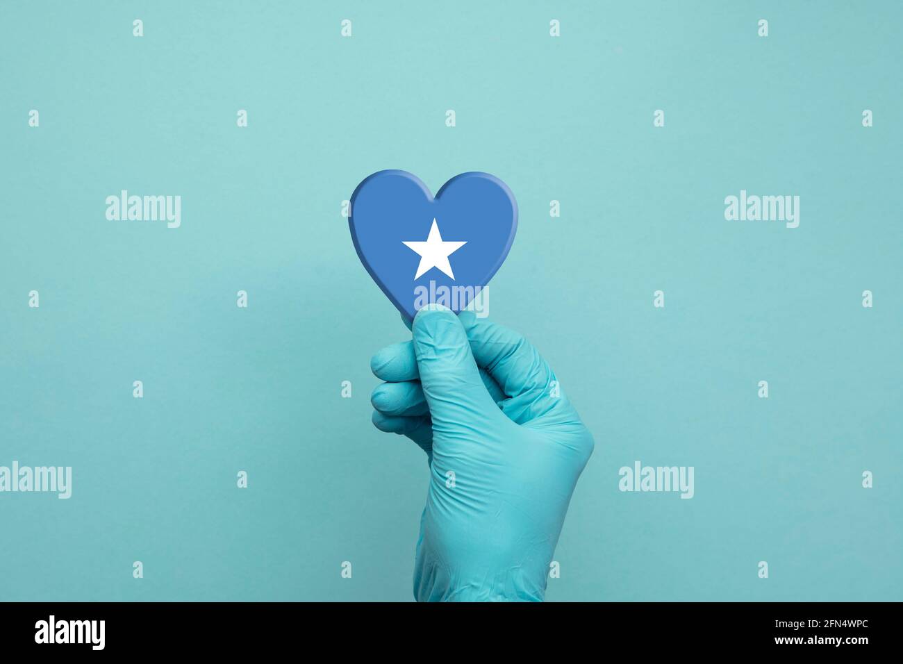 Mani che indossano guanti chirurgici protettivi che tengono il cuore della bandiera somala Foto Stock