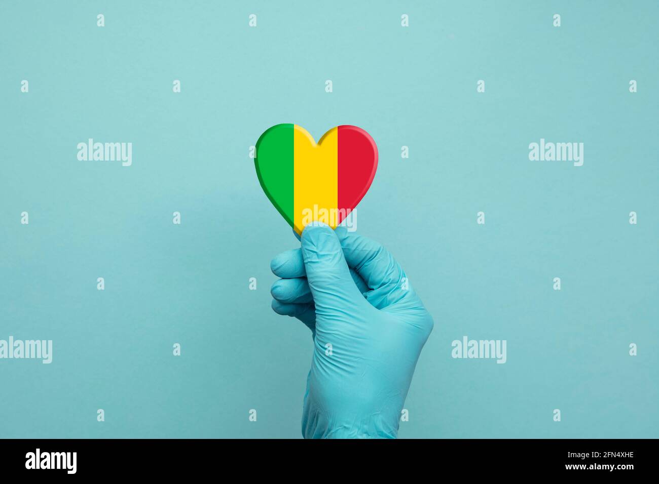 Mani che indossano guanti chirurgici protettivi che tengono il cuore della bandiera Mali Foto Stock