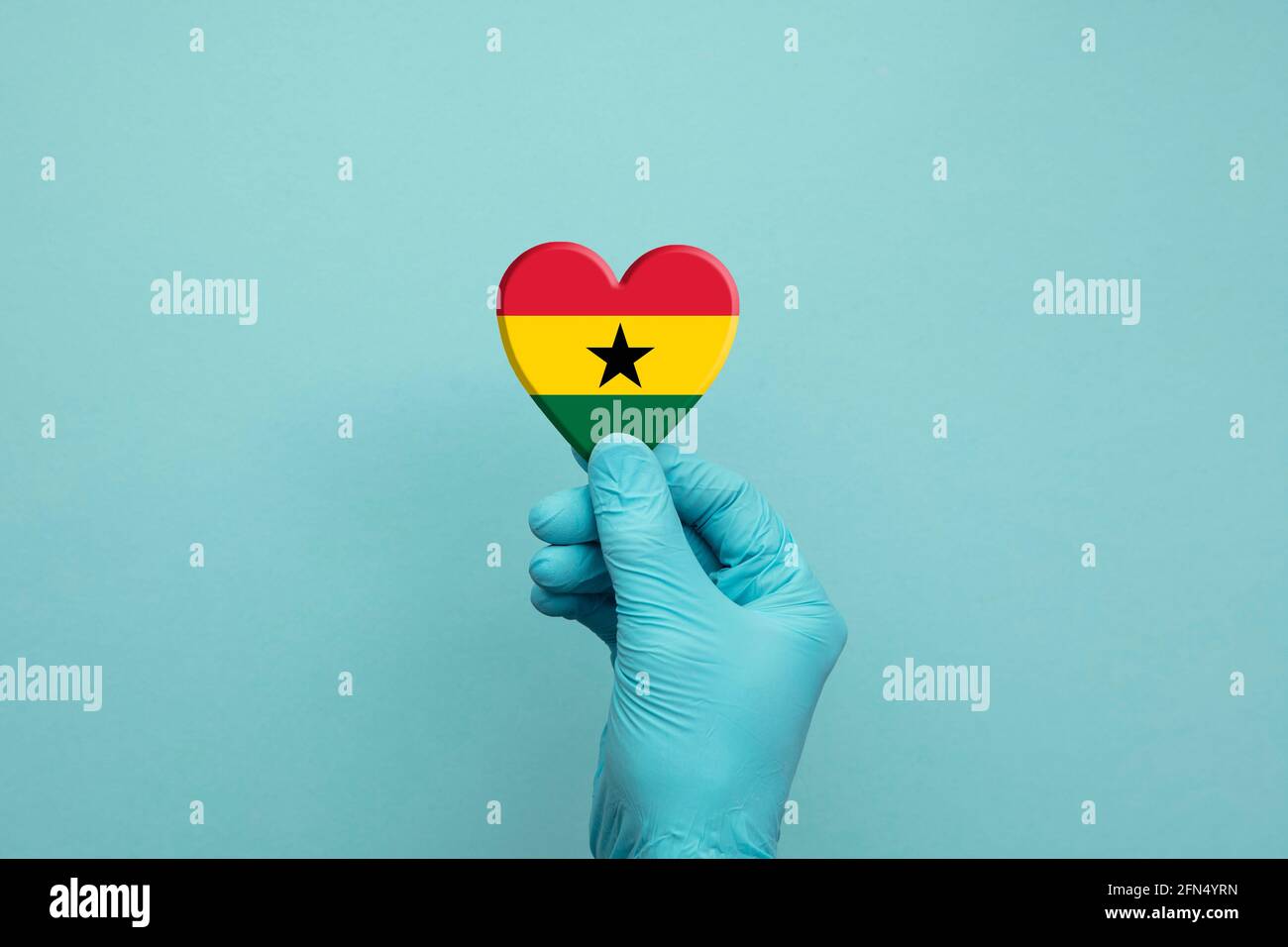 Mani che indossano guanti chirurgici protettivi che tengono il cuore della bandiera del Ghana Foto Stock