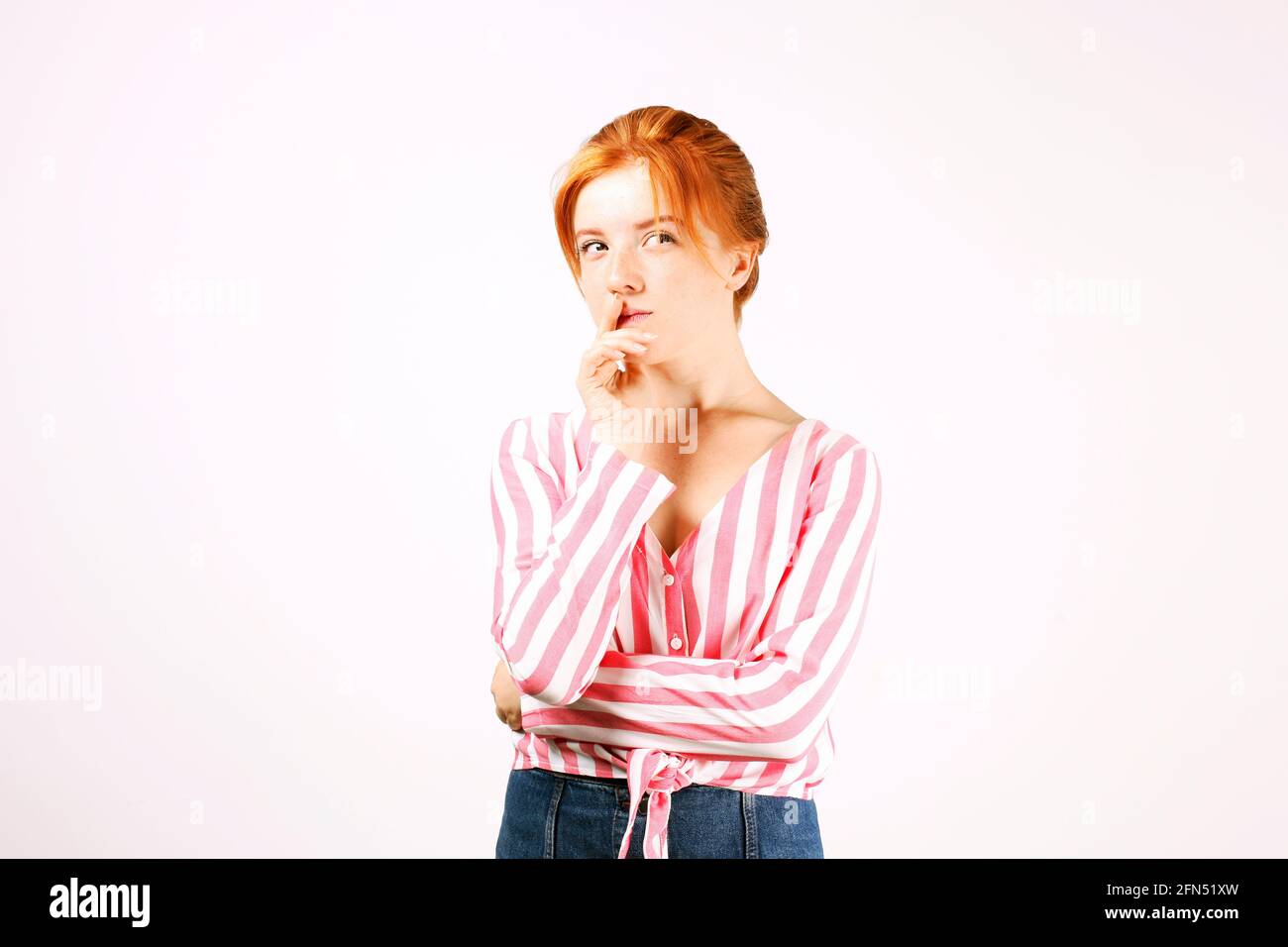 Giovane bella donna con lunghi capelli rossi naturali, pensando espressione facciale, mani sul sottiglietto posa. Bella donna testa rossa hipper pensieroso Foto Stock