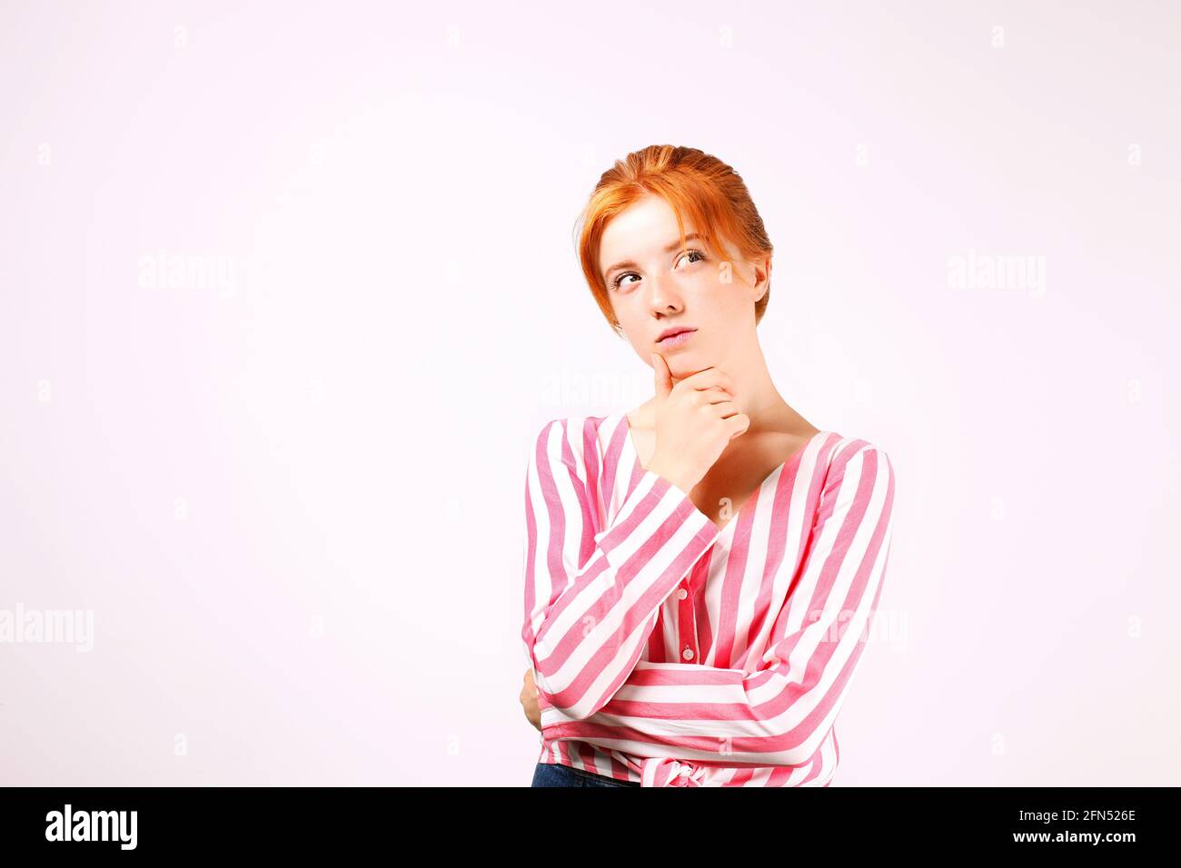 Giovane bella donna con lunghi capelli rossi naturali, pensando espressione facciale, mani sul sottiglietto posa. Bella donna testa rossa hipper pensieroso Foto Stock