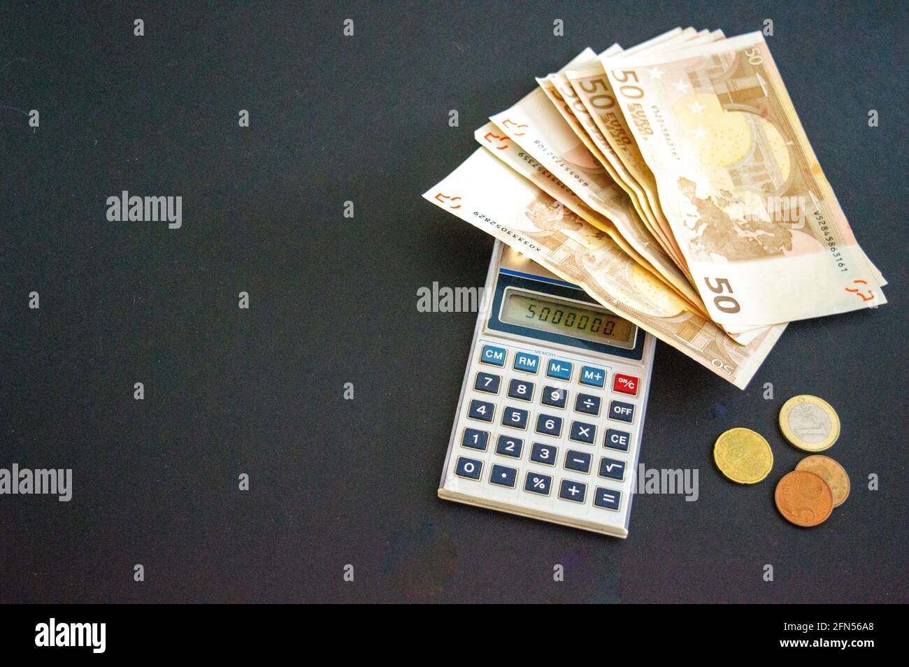 Calcolatrice con 50 banconote e monete in euro su sfondo grigio-nero. Spazio Foto Stock