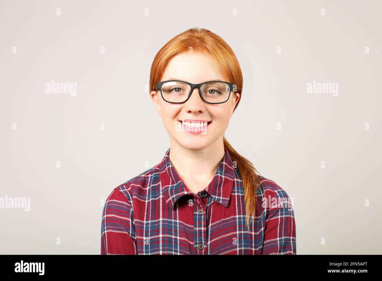 Primo piano ritratto di bella studentessa giovane donna college con capelli rossi che indossano occhiali neri cornice e camicia flanella. Rosso femmina sorridente. Redhea Foto Stock