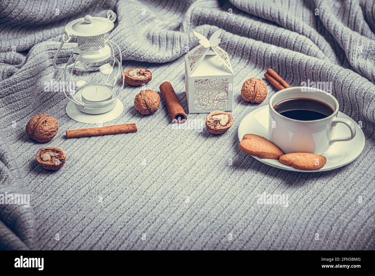 Una bella plaid, una tazza con caffè e biscotti su un tavolo con candele e una busta bianca. Foto Stock