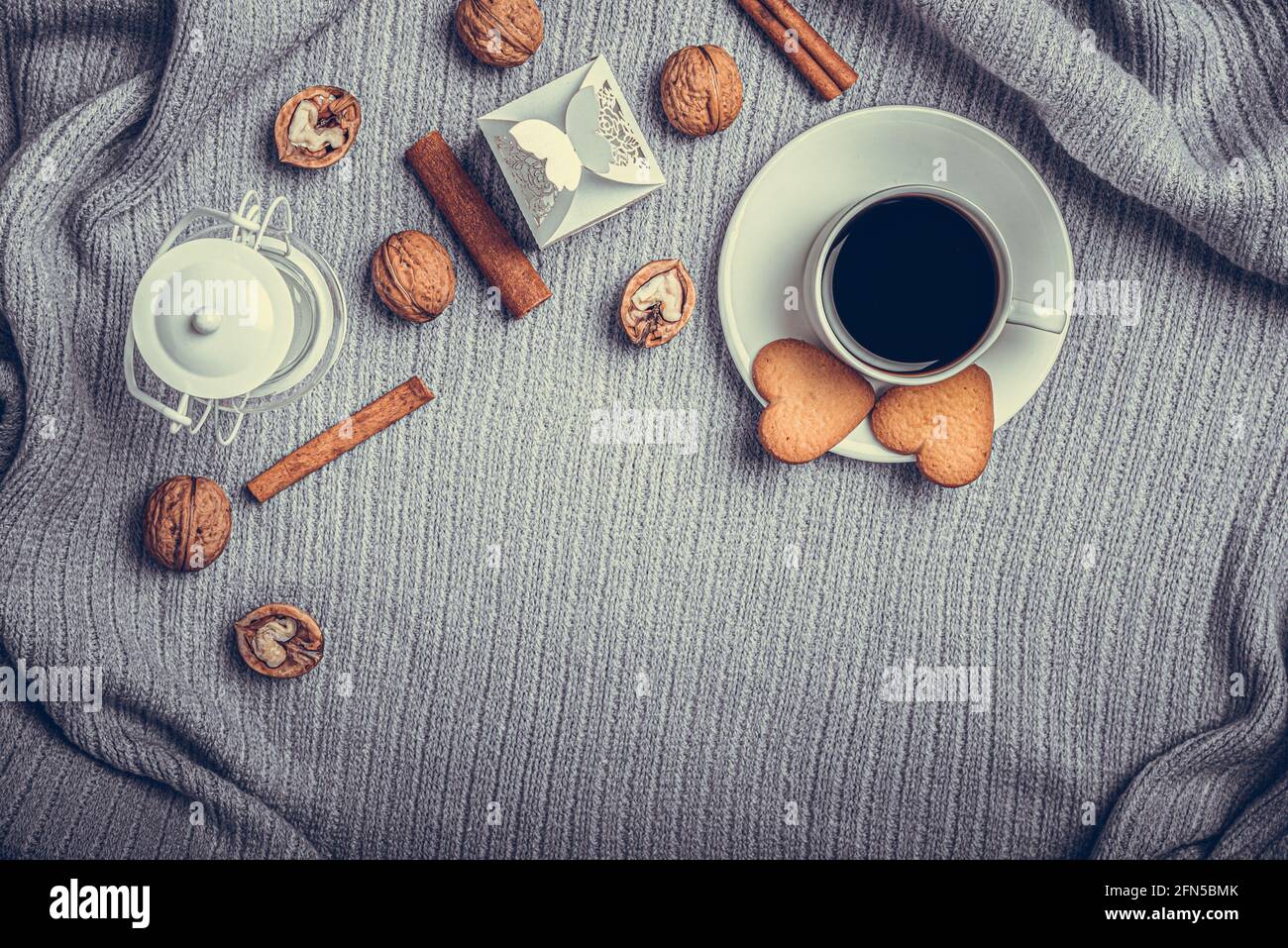 Una bella plaid, una tazza con caffè e biscotti su un tavolo con candele e una busta bianca. Foto Stock