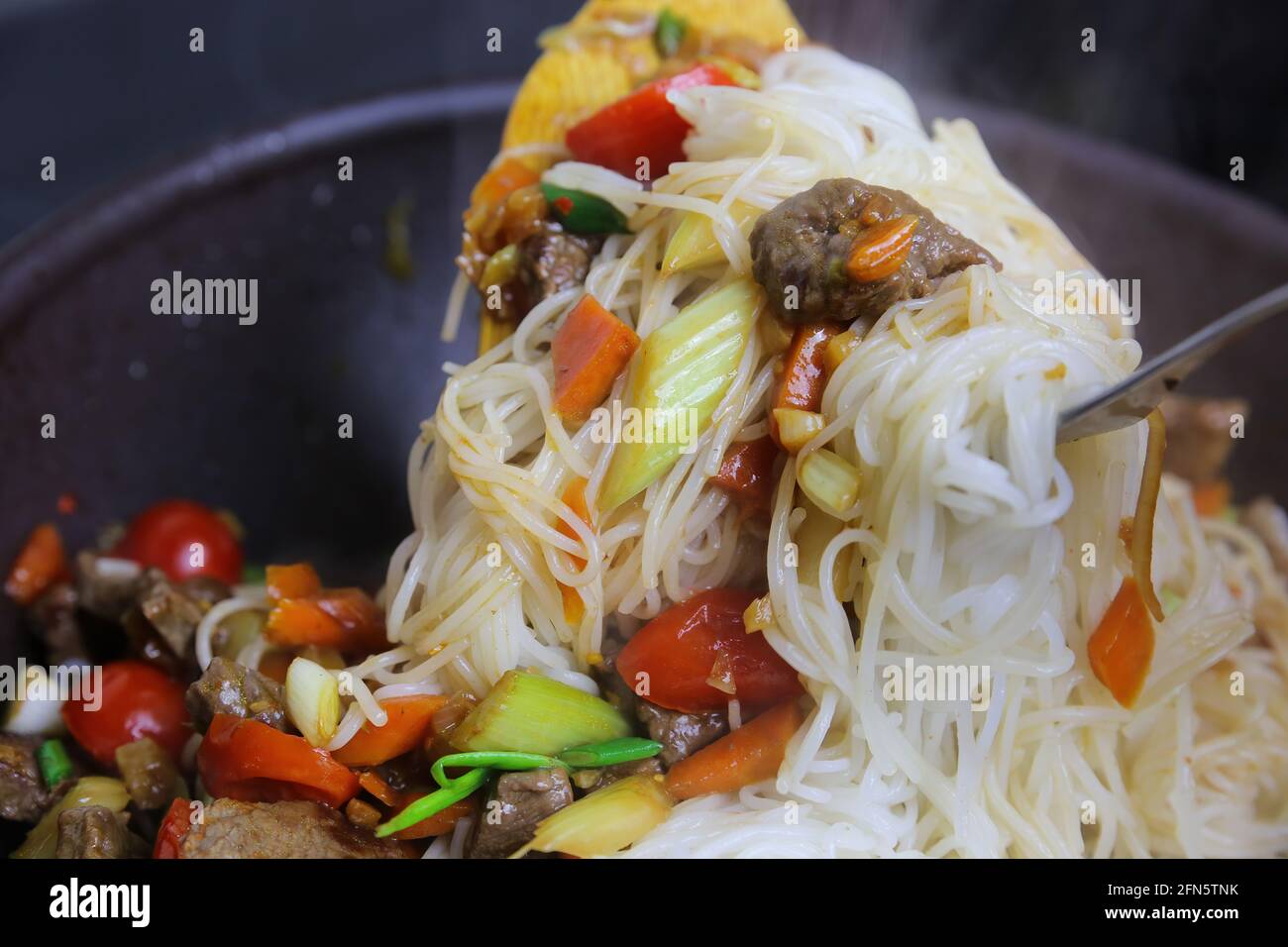 Closeup di tagliatelle di riso cucinate aggiunte al cibo cinese asiatico nel wok Foto Stock