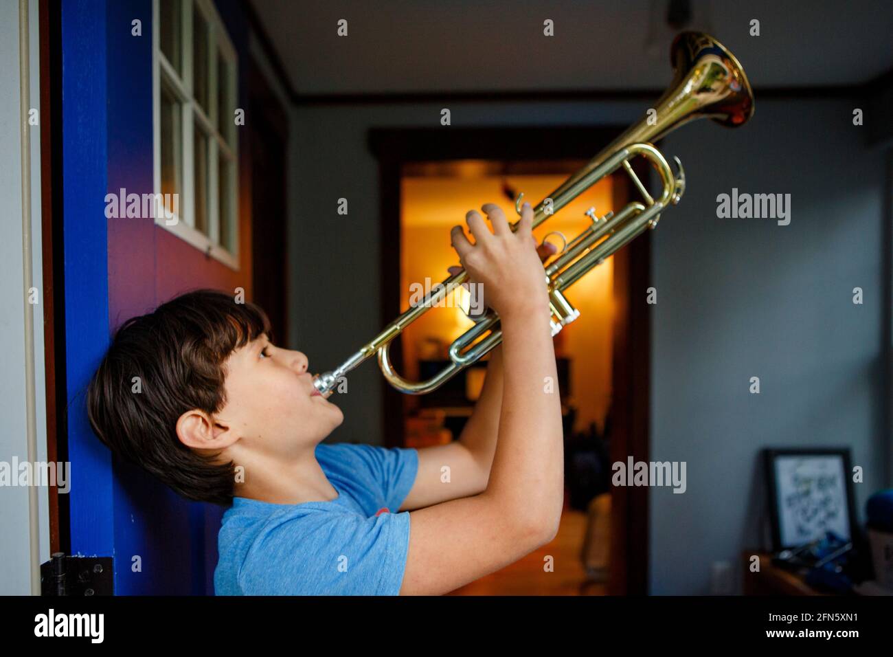 Un ragazzo sta in piedi in una porta aperta colorata che gioca a. tromba Foto Stock