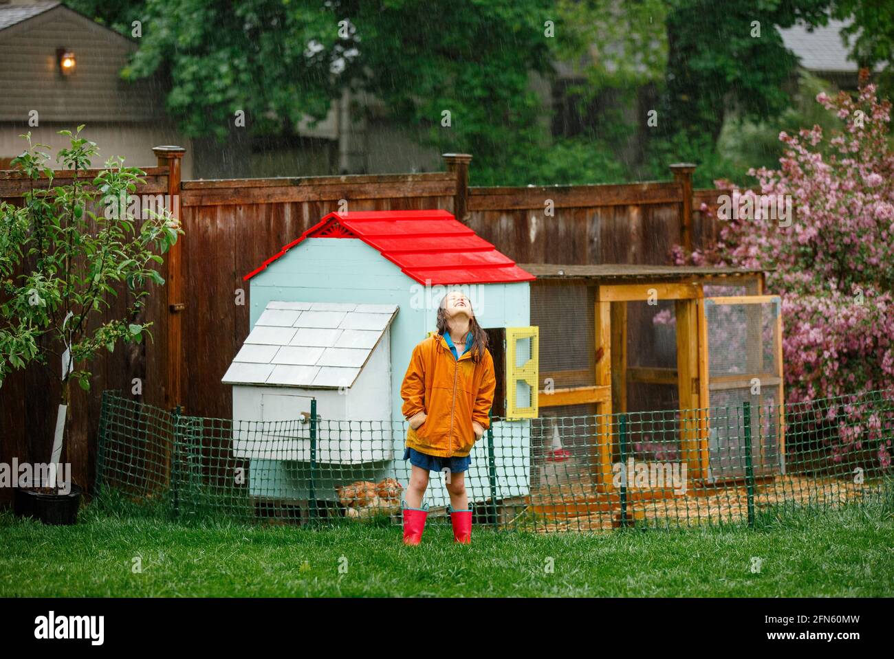 Un bambino gioioso sta in piedi nella pioggia in giardino vicino polpette di pollo guardando in su Foto Stock