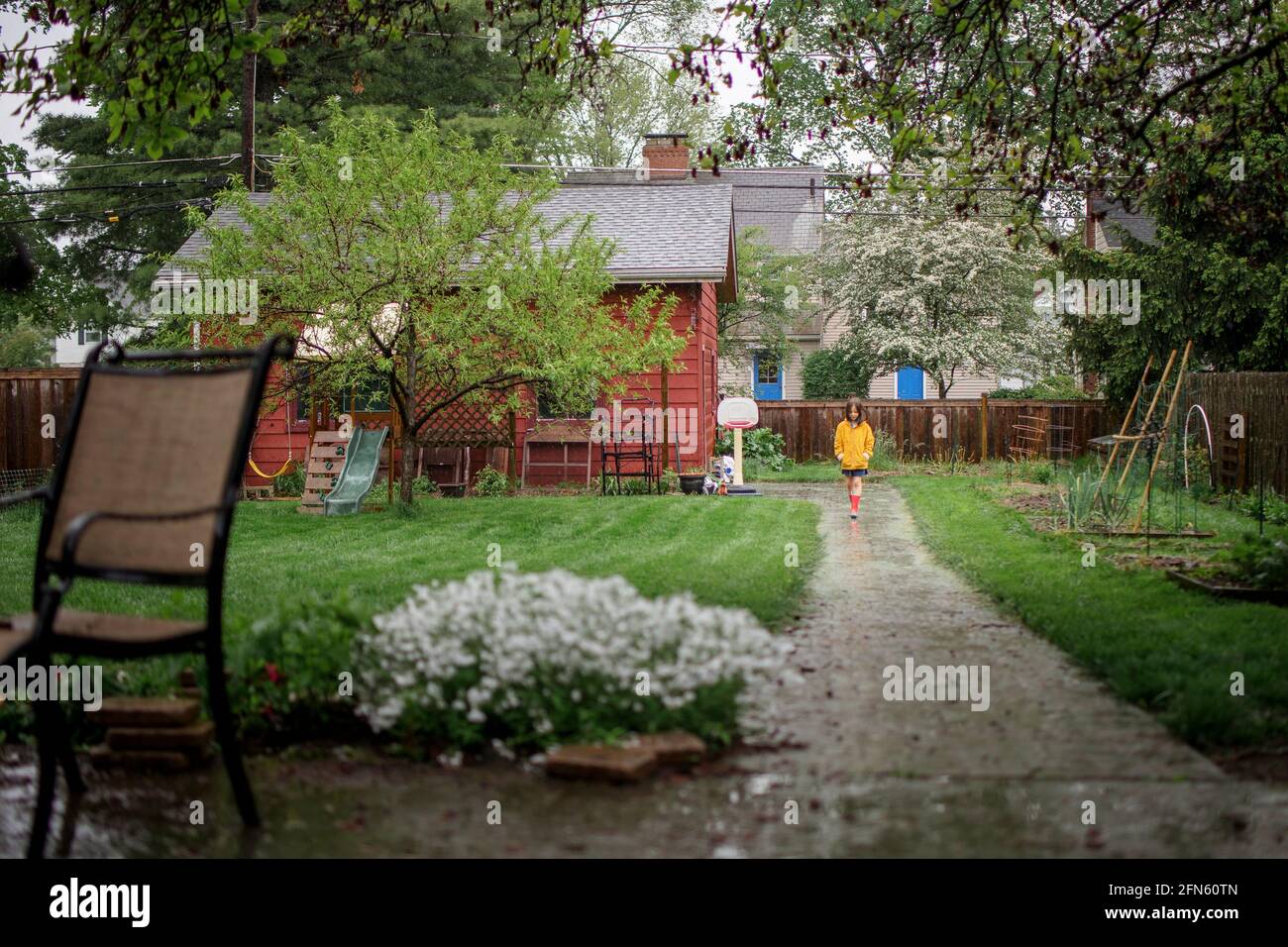 Un piccolo bambino cammina lungo il sentiero sotto la pioggia nel cortile giardino Foto Stock