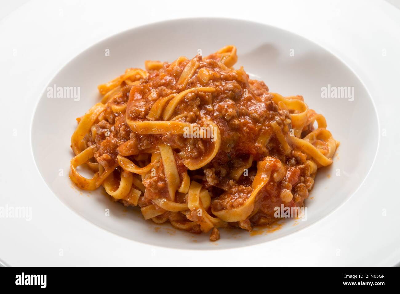 Tagliatelle italiane condite con salsa di carne e pomodoro, primo piano in un piatto bianco Foto Stock
