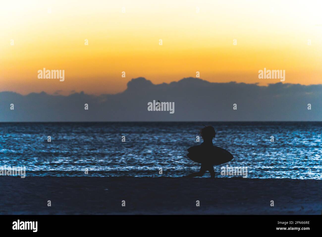 Il giovane corre lungo la spiaggia in silhouette con boogie board al tramonto. Foto Stock