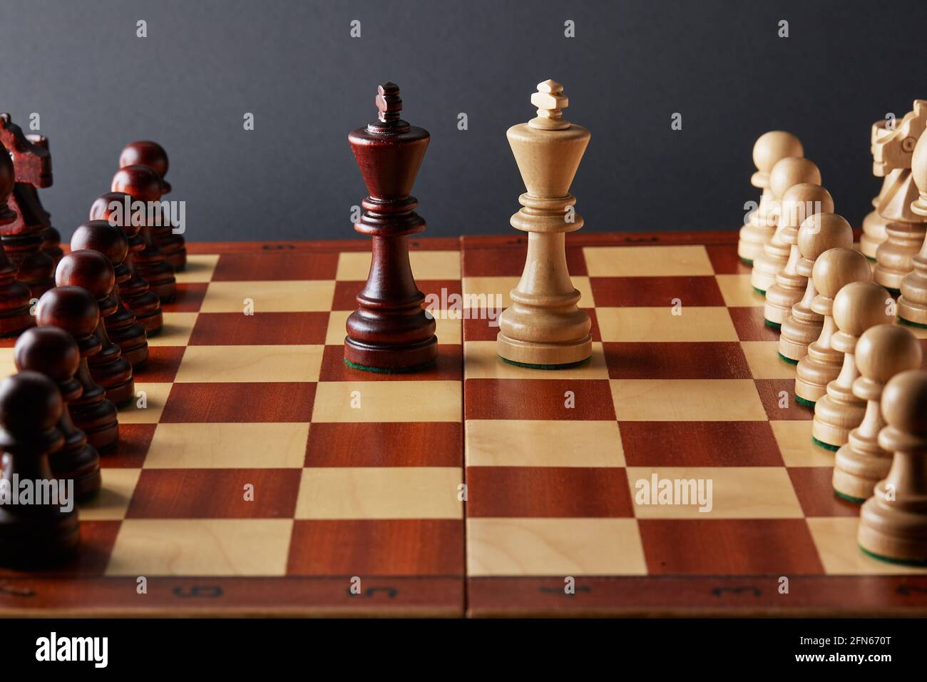 Classico torneo di scacchi in legno ambientato su sfondo nero. Due re al centro della tavola altri pezzi allineati Foto Stock