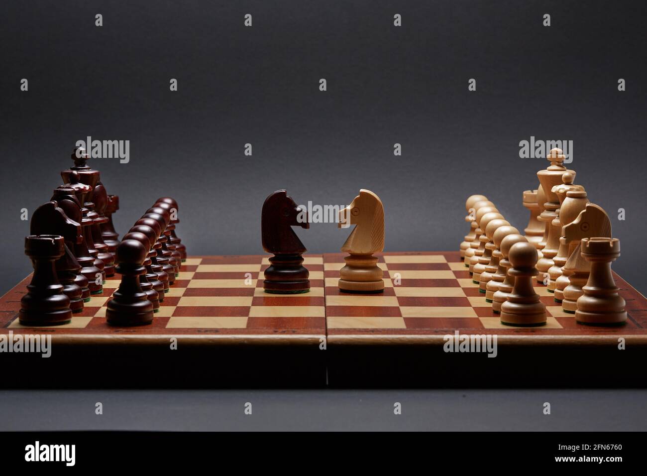 Classico torneo di scacchi in legno ambientato su sfondo nero. Due cavalieri al centro della tavola altri pezzi allineati Foto Stock
