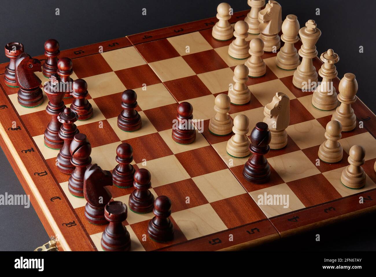 Classico torneo di scacchi in legno ambientato su sfondo nero. Scacchiera con pezzi. La disposizione dei pezzi deriva da un'apertura conosciuta come Gamb della Regina Foto Stock