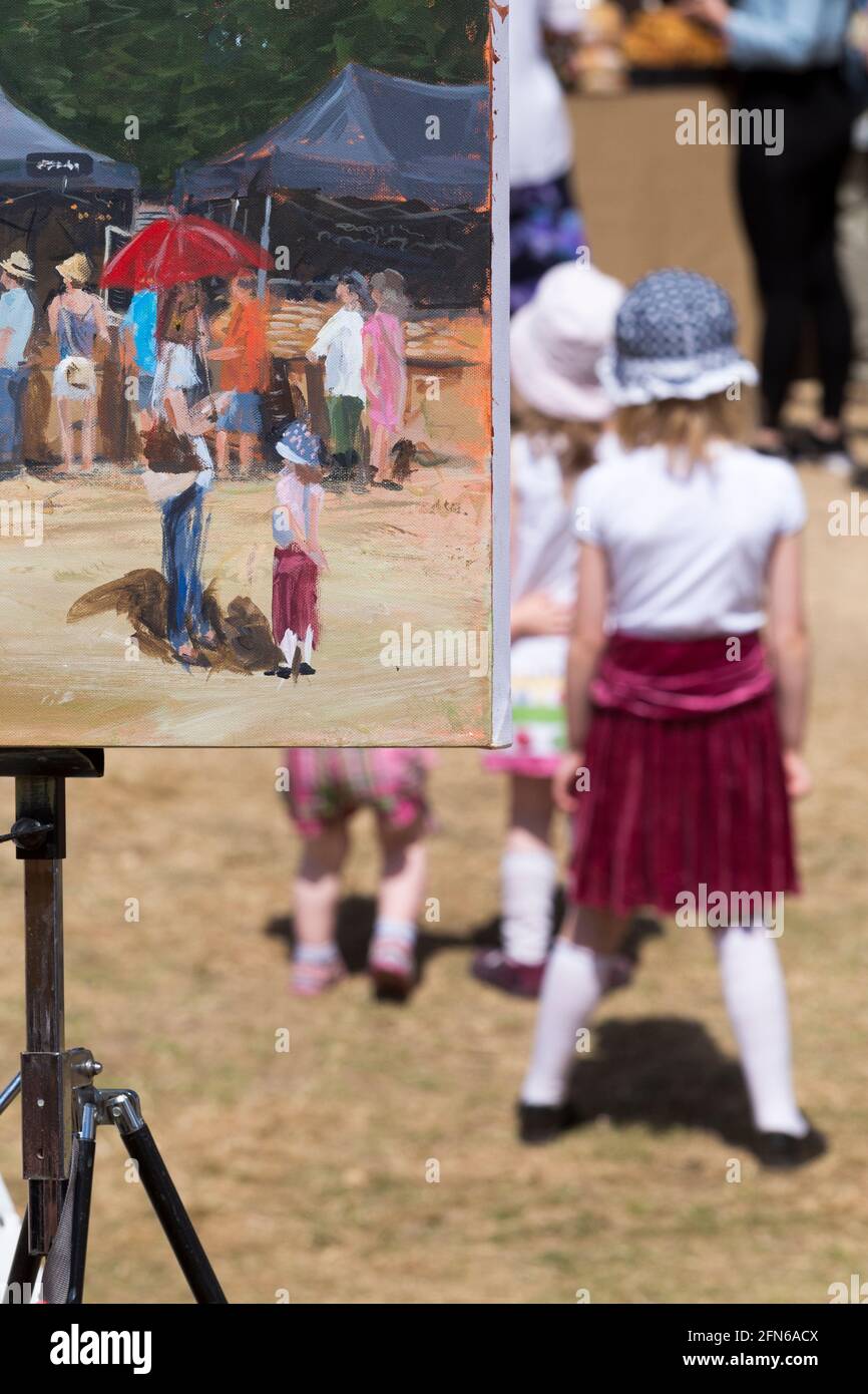 Artista che dipinge una scena in vernice, tra cui una ragazza in gonna rossa, in posa per il pittore. Il campo arabile di una fattoria che si è diversificata è stato riproposto temporaneamente per ospitare il festival. Giornate estive soleggiate con sole e cielo blu. UK (123) Foto Stock