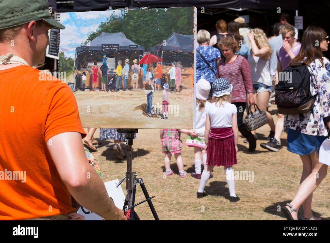 Artista che dipinge una scena in vernice, tra cui una ragazza in gonna rossa, in posa per il pittore. Il campo arabile di una fattoria che si è diversificata è stato riproposto temporaneamente per ospitare il festival. Giornate estive soleggiate con sole e cielo blu. UK (123) Foto Stock