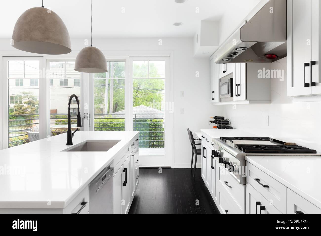 Un'elegante cucina bianca con elettrodomestici Thermador in acciaio inossidabile, grande isola con un piano di granito e moderne luci appese sopra. Foto Stock