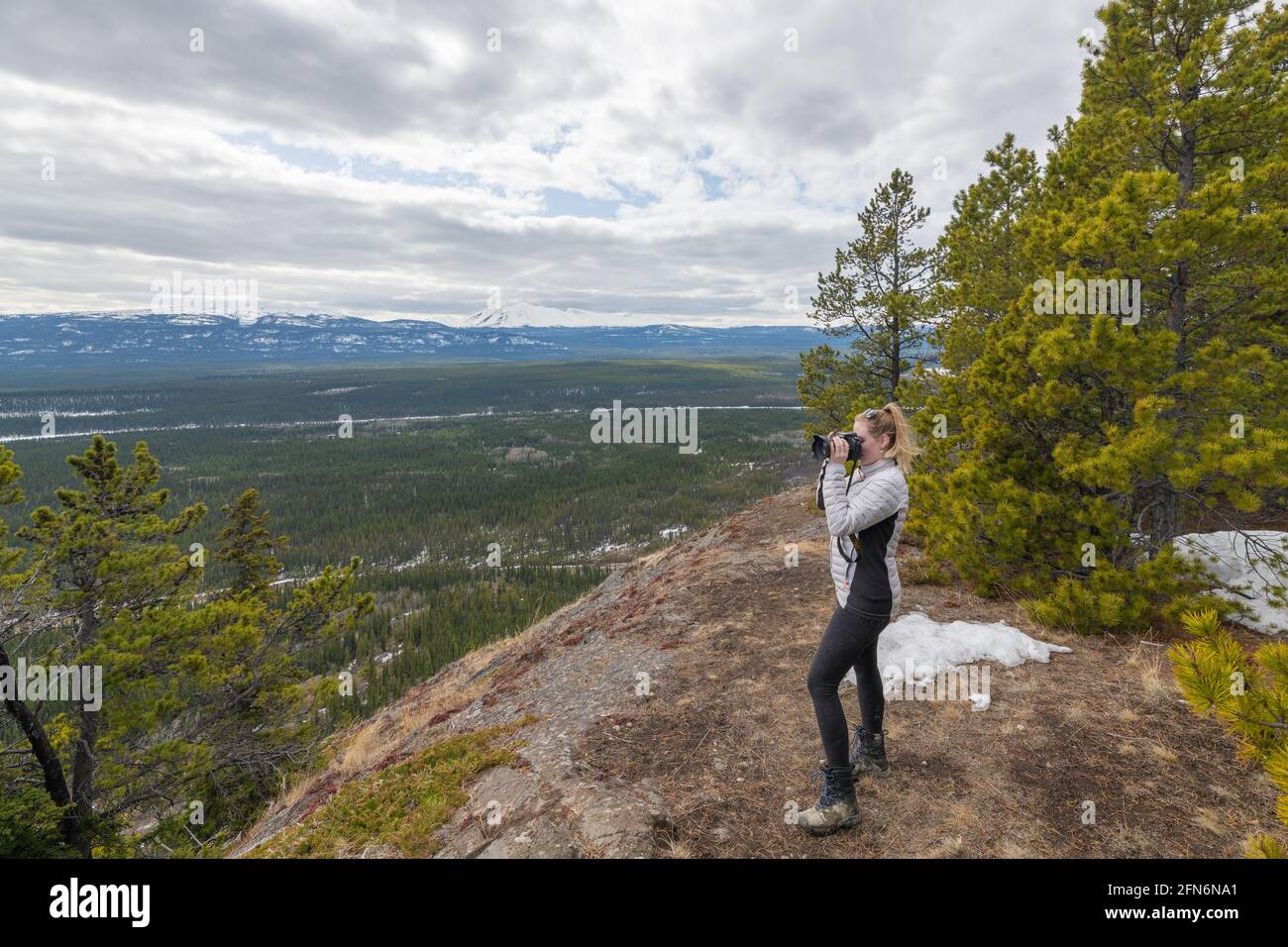 Donna con giacca bianca, pantaloni neri in piedi sul bordo di un sentiero escursionistico in cima alla montagna scattando foto, fotografando la vista panoramica a Yukon. Foto Stock