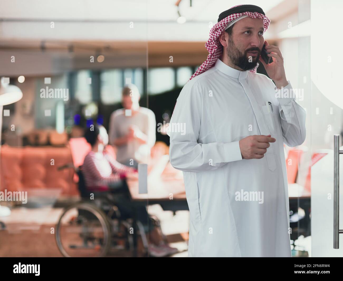 Uomo d'affari arabo mediorientale in ufficio che parla su smartphone davanti al suo team Foto Stock