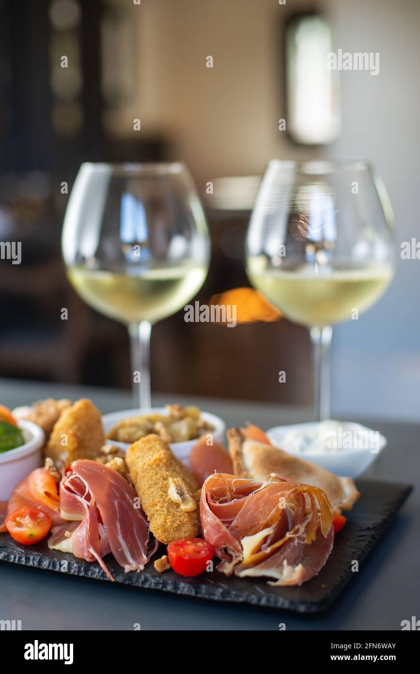 vassoio di prosciutto, e prodotti mediterranei acompanati da due tazze di vino bianco Foto Stock