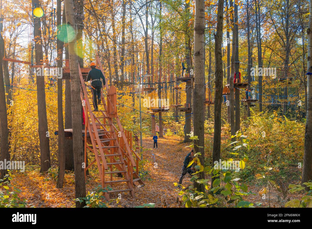 Kazan, Russia - 03 ottobre 2020: Un giovane in un casco sale una scala ad un albero in un parco divertimenti a corda, i bambini salgono gli alberi sotto i supervisi Foto Stock