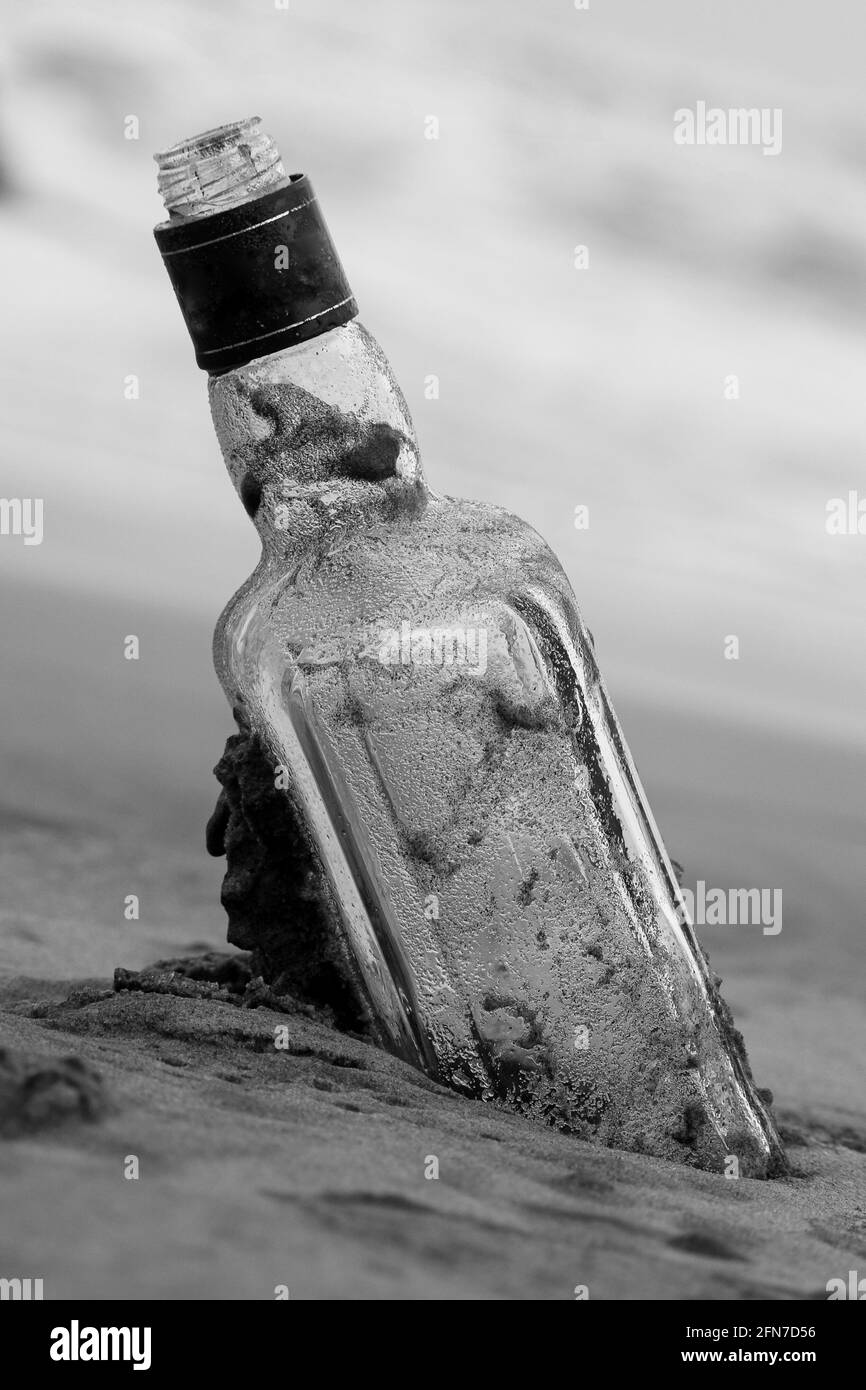 Fuoco selettivo di una bottiglia vuota sulla spiaggia di sabbia su uno sfondo sfocato Foto Stock