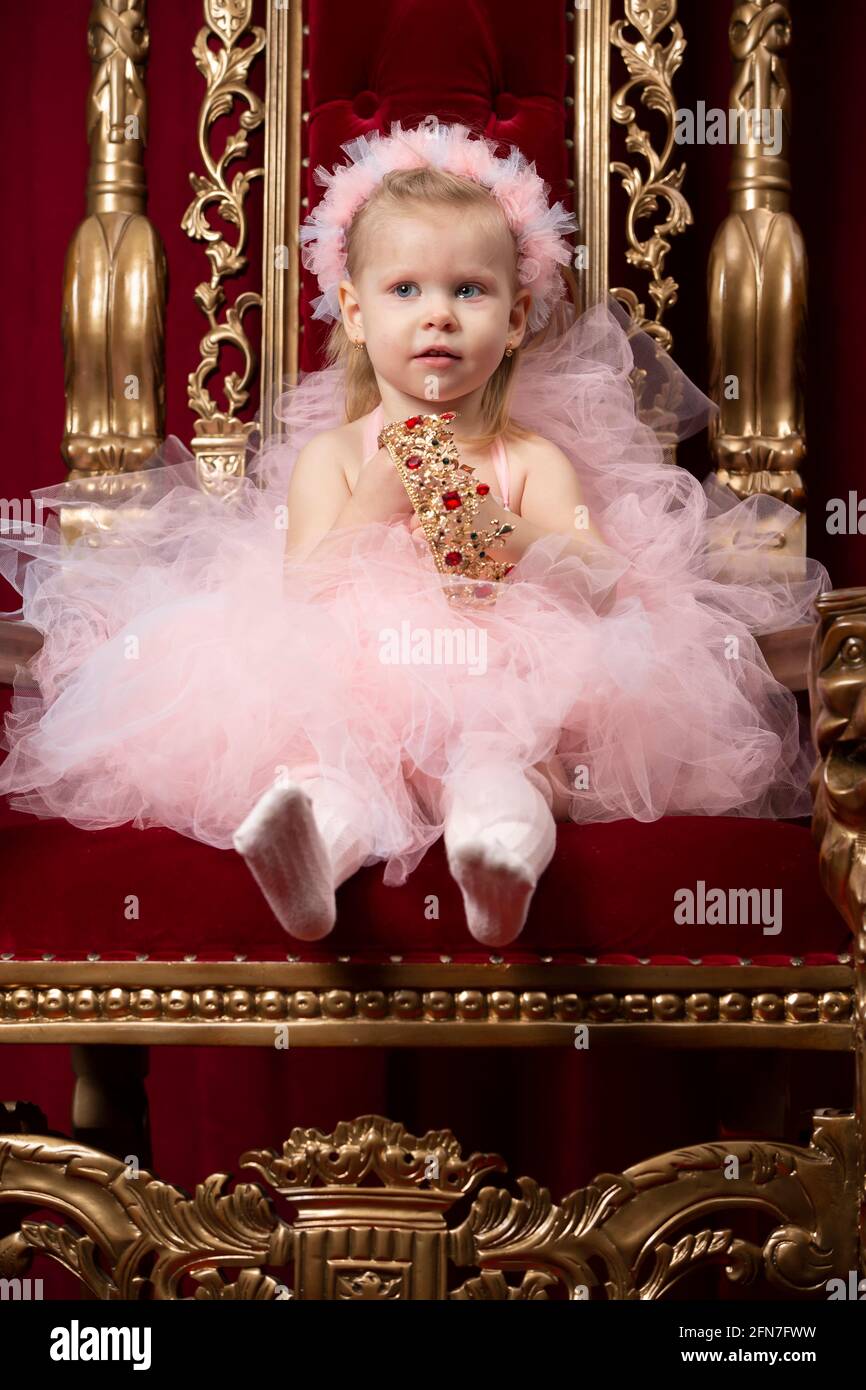 Una bambina divertente in un elegante abito rosa si siede in una lussuosa poltrona. Foto Stock