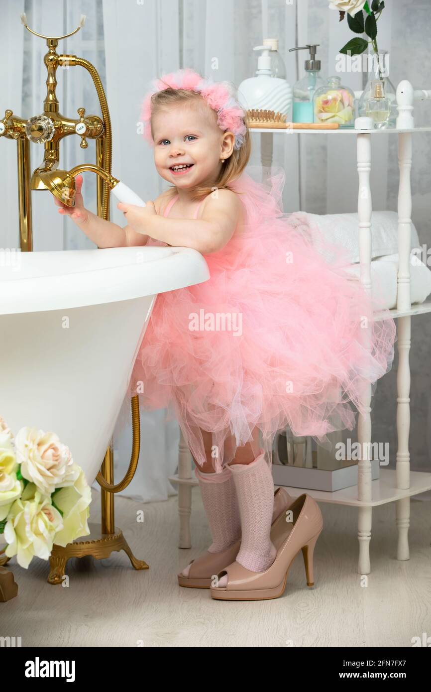 Una bambina divertente in rosa intelligente e tacchi alti si trova in bagno e ride .. Foto Stock