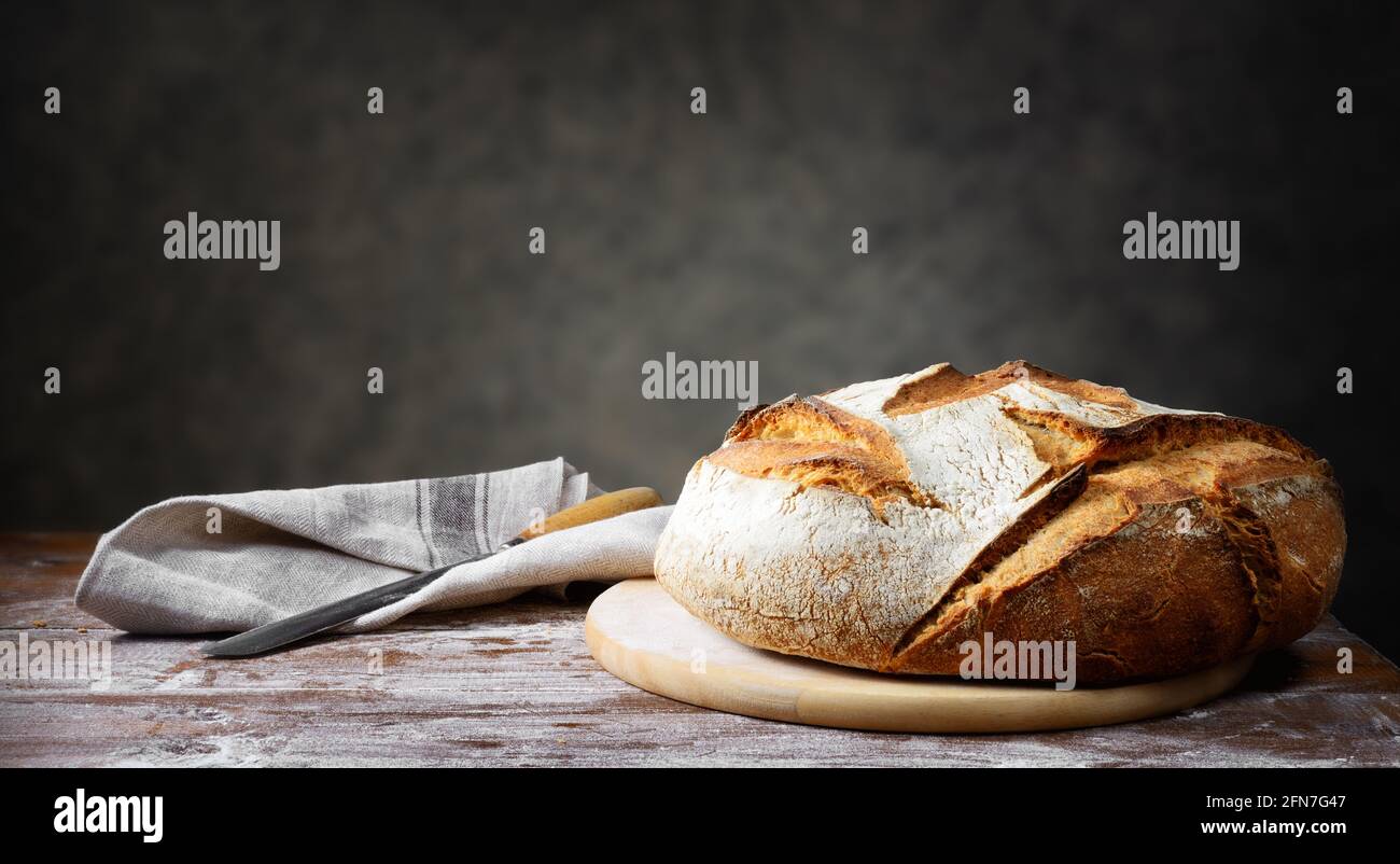 Pane di pane tradizionale con coltello, tovagliolo e tagliere su tavolo in legno rustico. Sfondo grigio, spazio per il testo. Foto Stock