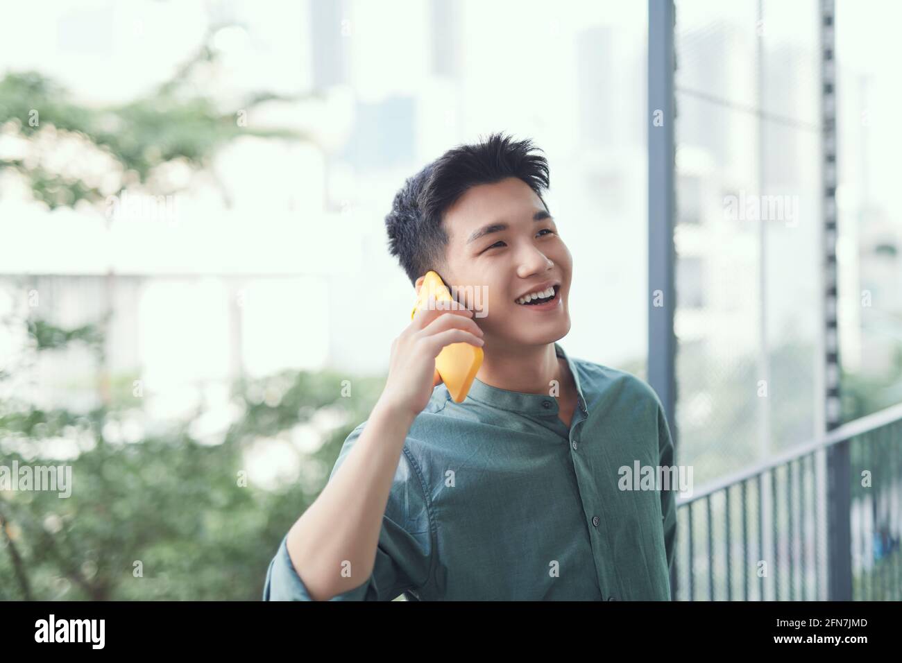 Uomo asiatico che parla su smartphone sorridendo ridendo forte rilassante al balcone Foto Stock