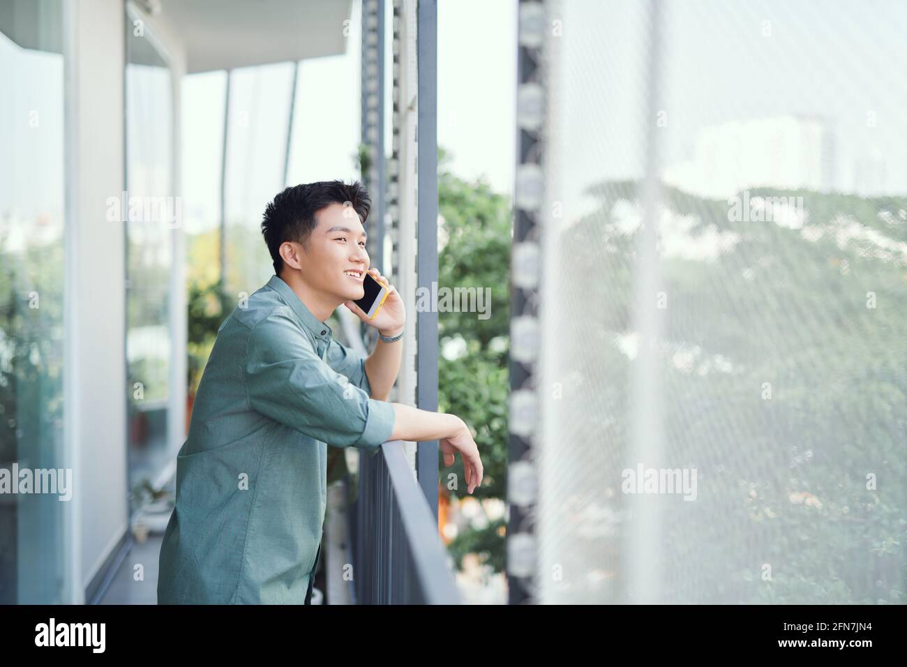 Uomo asiatico che parla su smartphone sorridendo ridendo forte rilassante al balcone Foto Stock