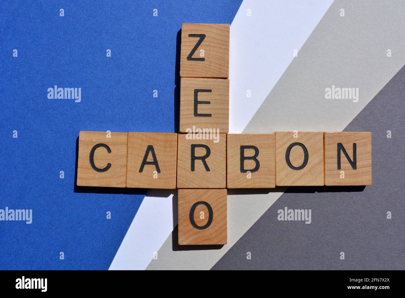 Zero, carbonio, parole in lettere alfabetiche in legno in forma di croceparola isolate su sfondo blu e grigio Foto Stock