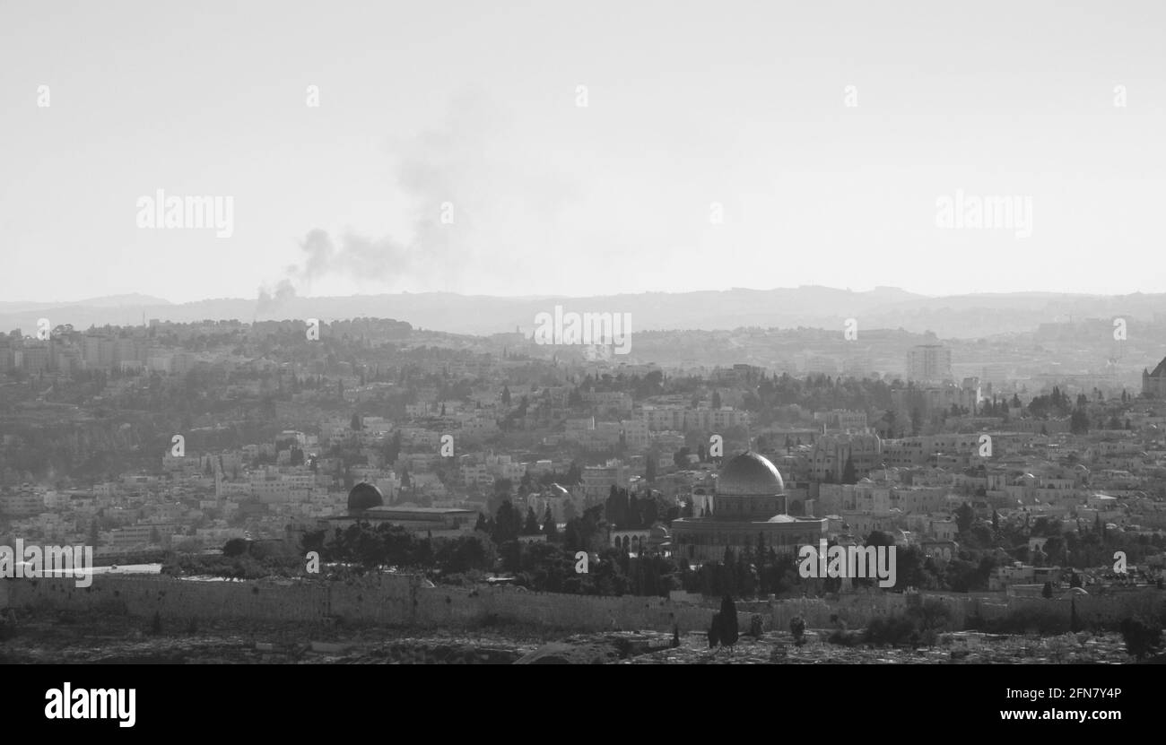 Una vista su n tetti della Città Vecchia di Gerusalemme e cupola dorata della roccia dal Monte Scopus. Foschia. Fumo di fuoco che si alza sullo sfondo. Foto in bianco e nero Foto Stock