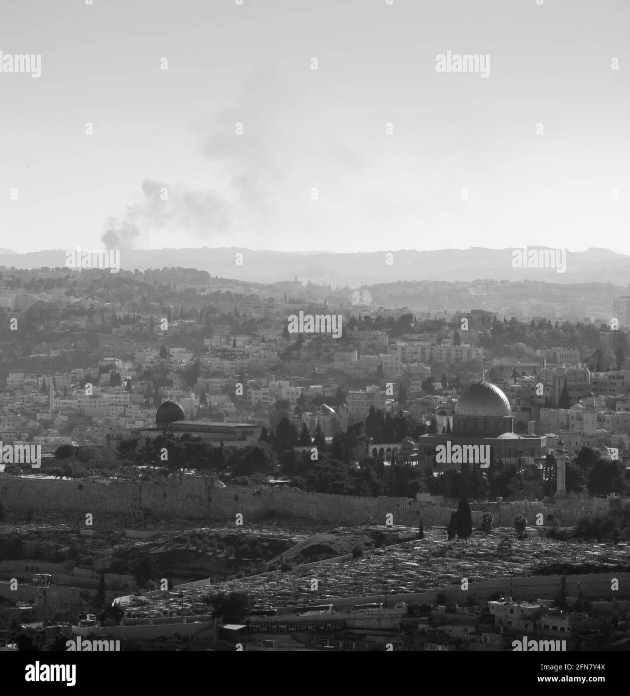 Una vista su n tetti della Città Vecchia di Gerusalemme e cupola dorata della roccia dal Monte Scopus. Foschia. Fumo di fuoco che si alza sullo sfondo. Foto in bianco e nero Foto Stock