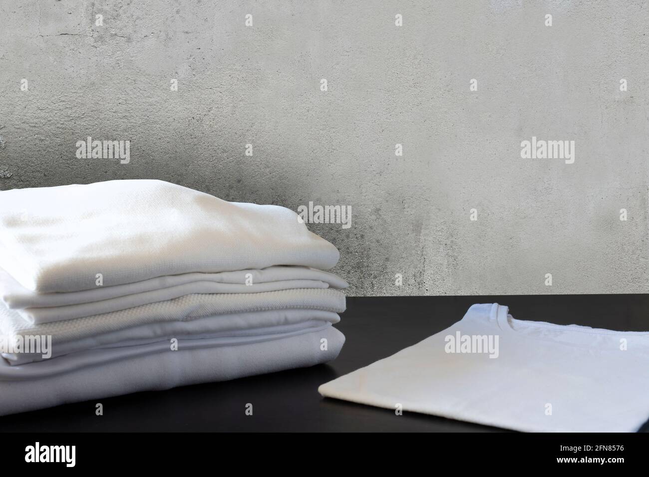 Pila di vestiti bianchi di fronte al muro di cemento e. sul pavimento nero Foto Stock