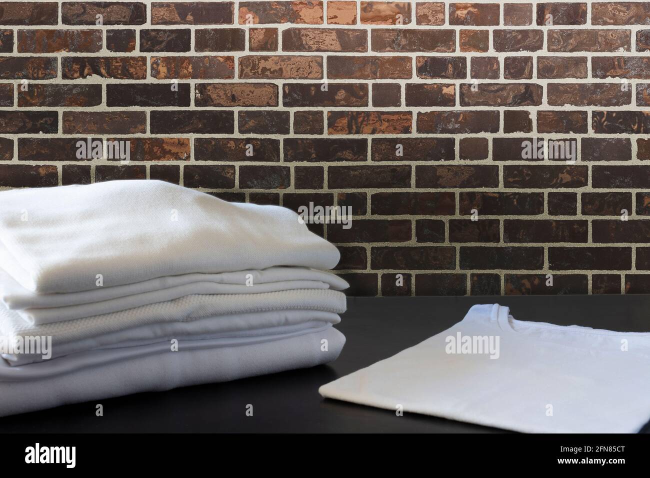 pila di vestiti bianchi ripiegati in piedi davanti a un muro di mattoni Foto Stock