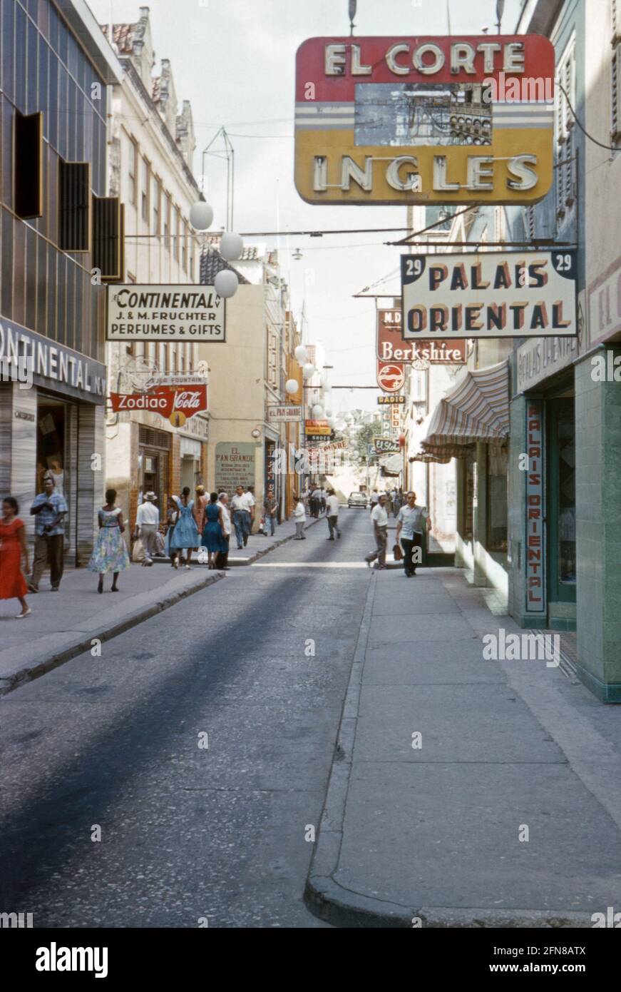 Una strada secondaria, Heerenstraat, a Willemstad, Curao alla fine degli anni '50. Willemstad è la capitale di Curao, un'isola del sud dei Caraibi che è un territorio olandese. Il centro della città, con la sua architettura unica, è un sito patrimonio dell'umanità dell'UNESCO. La lingua parlata è Papiamento, una lingua portoghese, anche se le insegne per la strada sono un mix di principalmente spagnolo e inglese. Oggi la strada è pedonale e gli edifici dipinti in colori luminosi 'patrimonio'. Questa immagine proviene da una vecchia trasparenza amatoriale del colore – una fotografia d'epoca degli anni '50. Foto Stock
