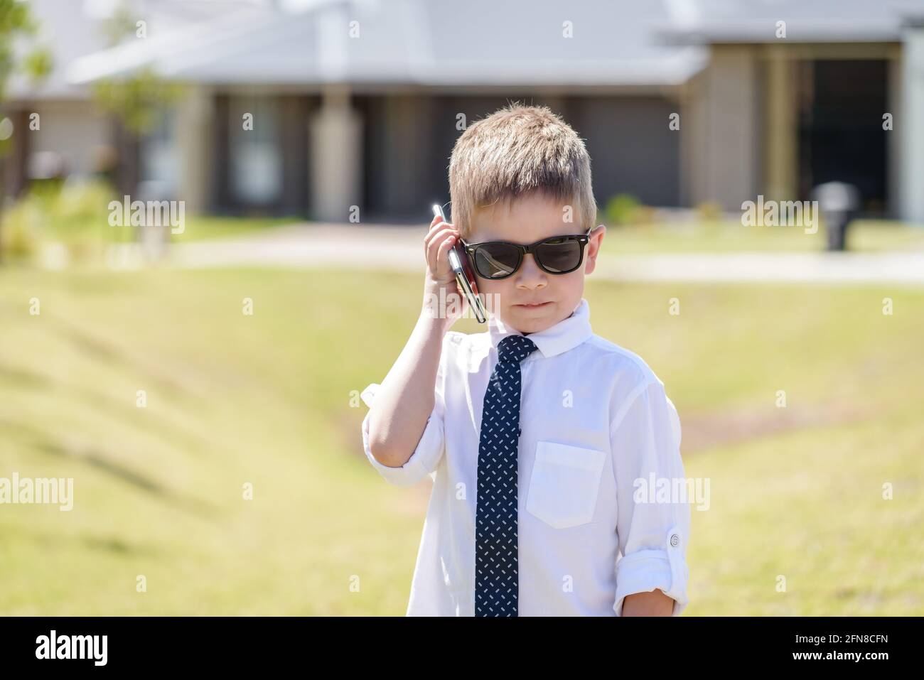 Carino ragazzo australiano che indossa abbigliamento da lavoro con occhiali da sole mentre si utilizza un telefono cellulare in una giornata estiva brillante Foto Stock