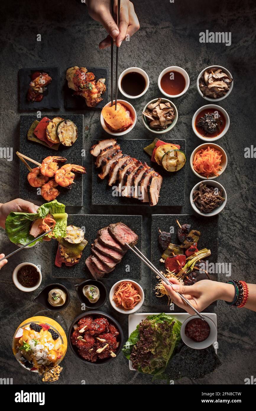 Disposizione piatta di un tavolo da barbecue coreano con le mani della gente selezionare il loro cibo Foto Stock