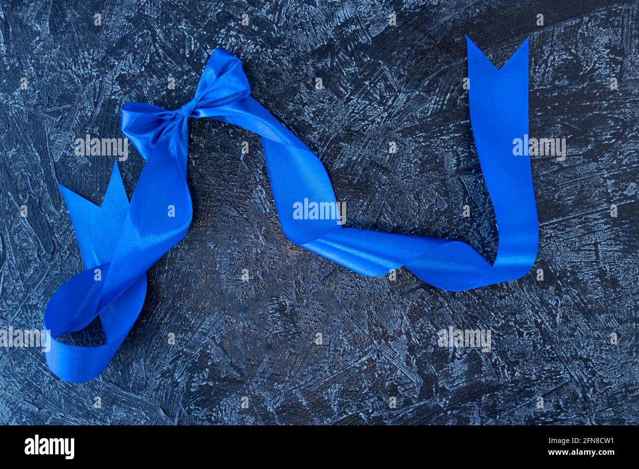 arco blu con un nastro su sfondo nero testurizzato. Messa a fuoco morbida. Vista dall'alto Foto Stock