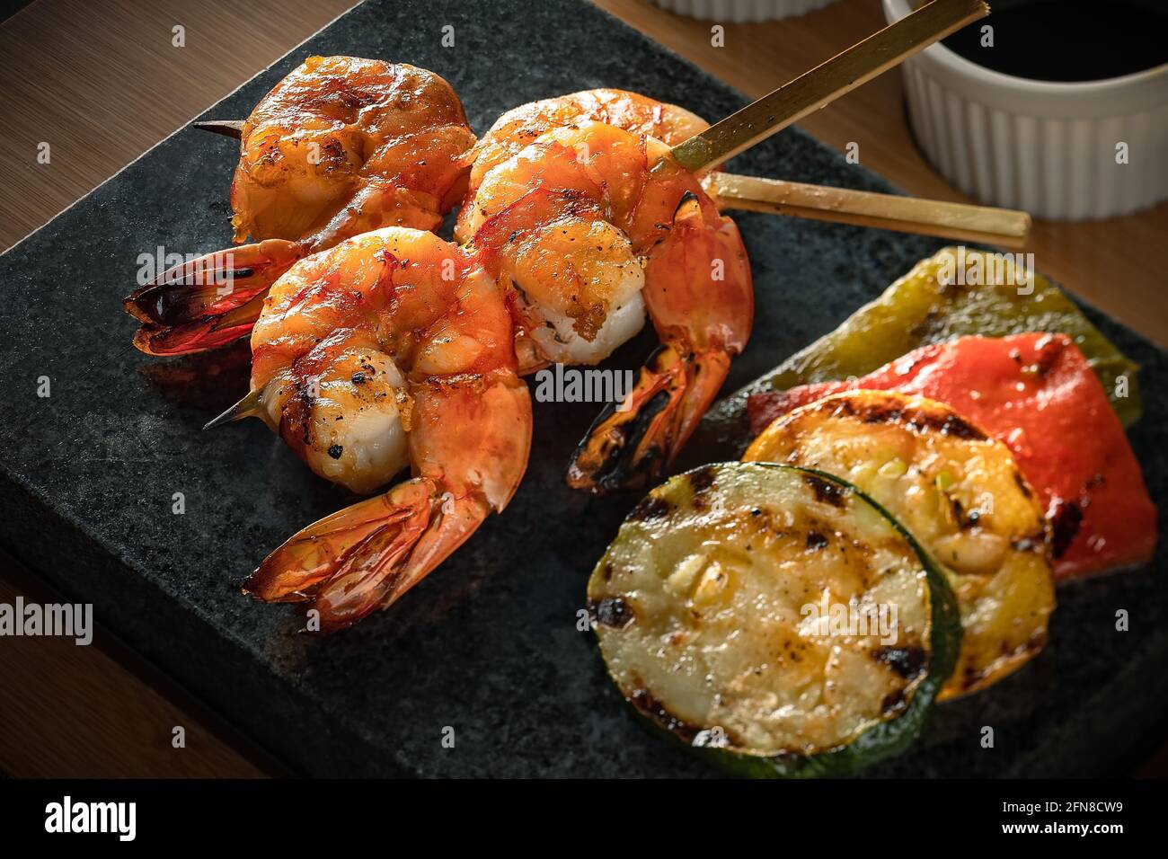 Primo piano su spiedini di gamberi serviti con zucchine alla griglia, peperoni rossi e peperoni verdi su un piatto scuro, buona selezione di piatti barbecue coreani Foto Stock