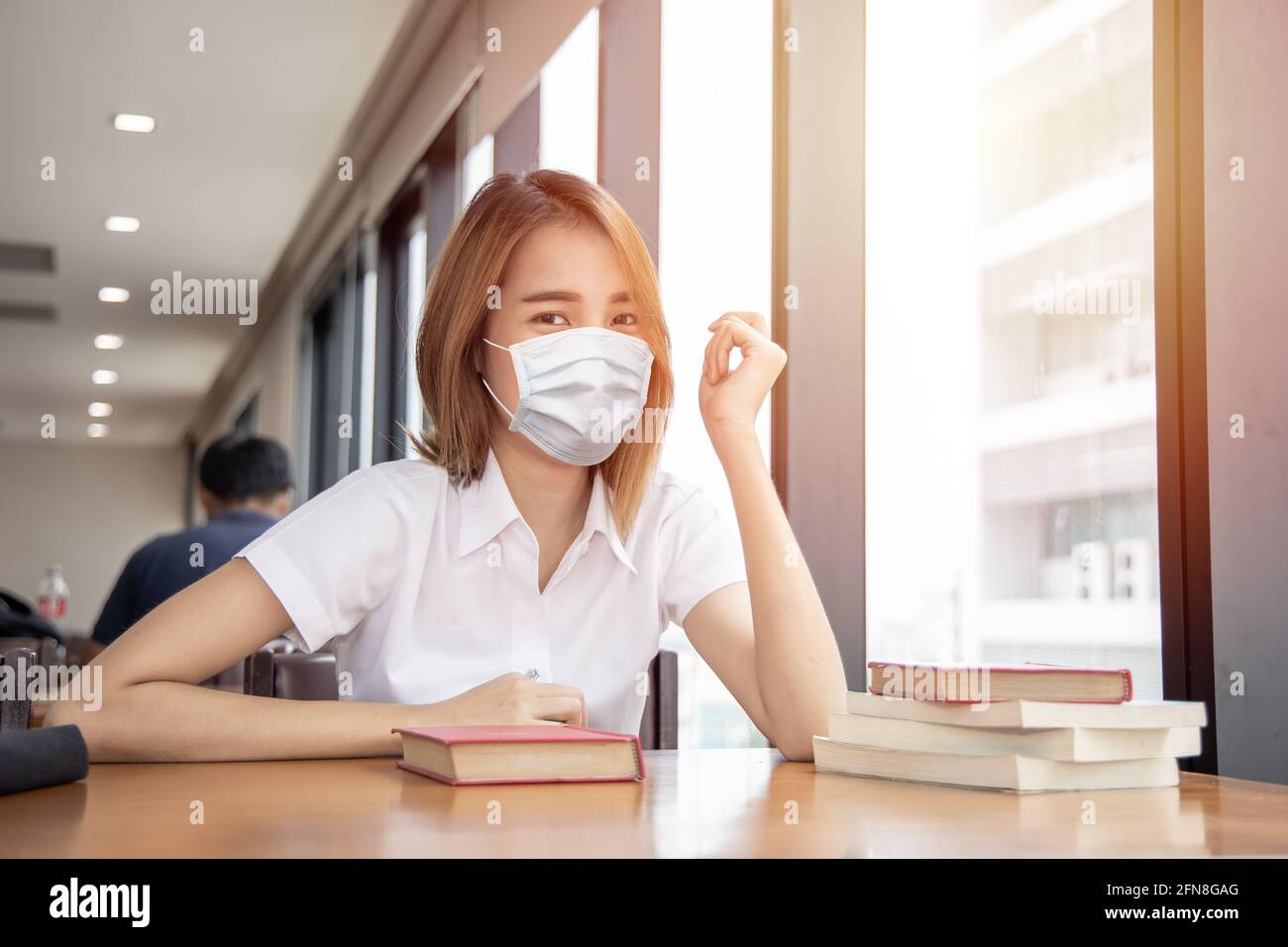 Asian Thai University ragazza teen Waring maschera viso per la salute prevenire covid in biblioteca. Foto Stock