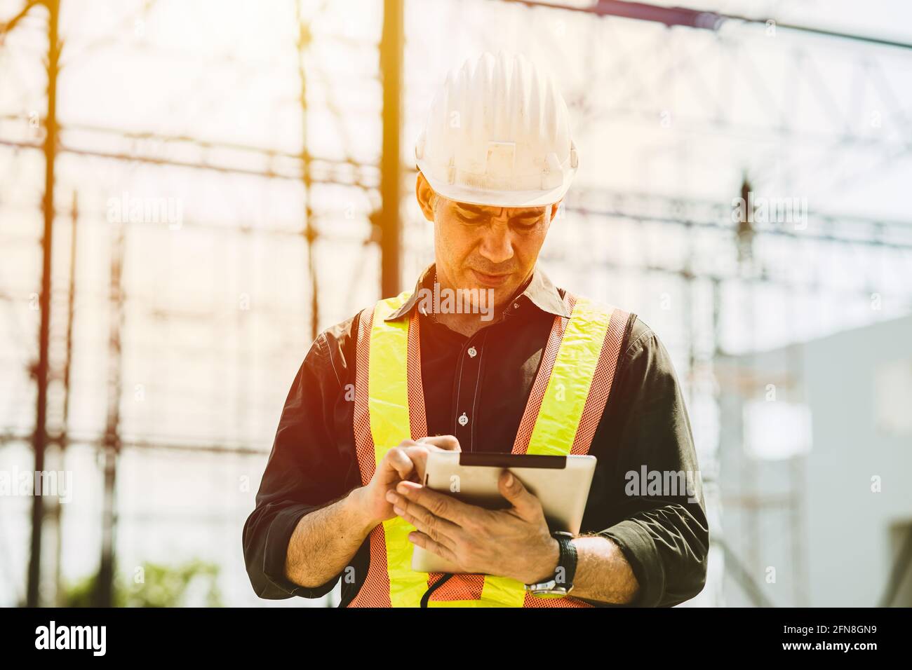 Il lavoratore del costruttore del caposquadra utilizza un computer tablet per controllare la pianificazione del pavimento dell'edificio nel cantiere. Foto Stock