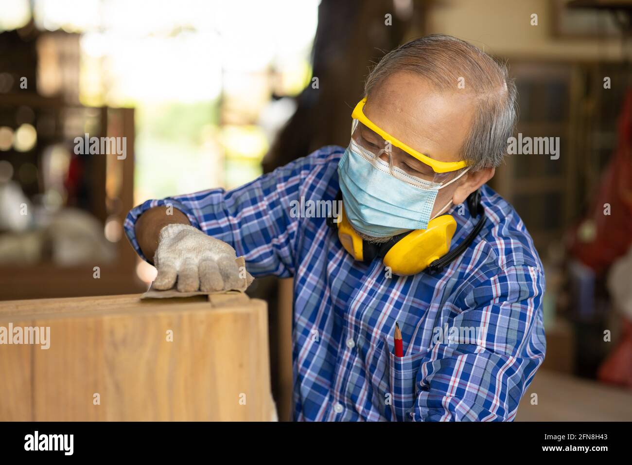 Anziano lavoratore legno woodcraft ritire hobby per il buon pensionamento, asiatico maschio maturo maestro professionale di fare mobili in legno con maschera protects viso Foto Stock