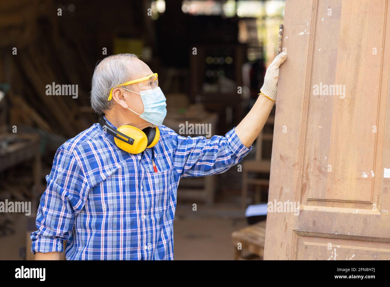 Anziano lavoratore legno woodcraft ritire hobby per il buon pensionamento, asiatico maschio maturo maestro professionale di fare mobili in legno con maschera protects viso Foto Stock